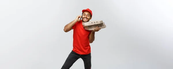 Levering Concept - portret van knappe African American Pizza delivery man op telefoon met klant. Geïsoleerd op grijs studio achtergrond. Kopiëren van ruimte. — Stockfoto