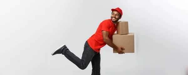 Conceito de entrega - Bonito afro-americano entrega homem corrida para entregar um pacote para o cliente. Isolado no estúdio Grey Background. Espaço de cópia . — Fotografia de Stock