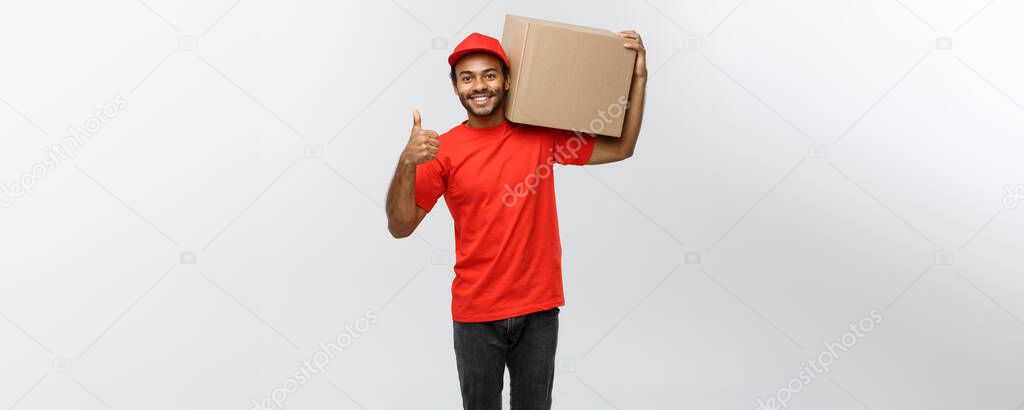 Delivery Concept - Portrait of Happy African American delivery man holding a box package and showing thumps up. Isolated on Grey studio Background. Copy Space.