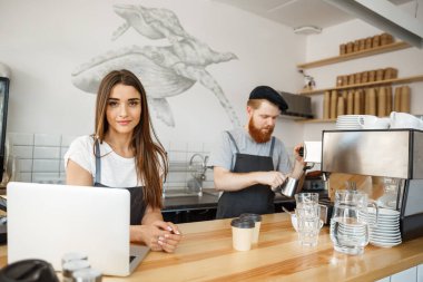 Kahve iş kavramı - pozitif genç sakallı dostum ve güzel çekici Bayan barista çift birlikte modern kahve dükkanında çalışmaktan hoşlanıyor