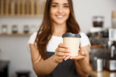 Kahve iş kavramı - kameraya gülümseyen güzel beyaz Bayan modern kahve dükkanında tek kullanımlık take away sıcak kahve sunmaktadır.