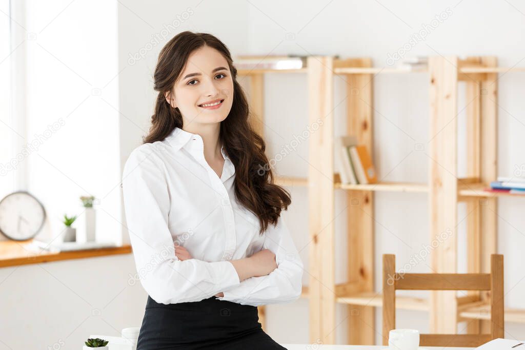 Smiling mature professional businesswoman with arms crossed sitting on the desk in office.