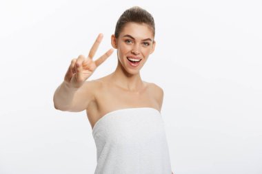 Yakın çekim güzel genç kadının göğüsleri gri, kaplama banyo havlusu ile iki parmak işareti gösterir