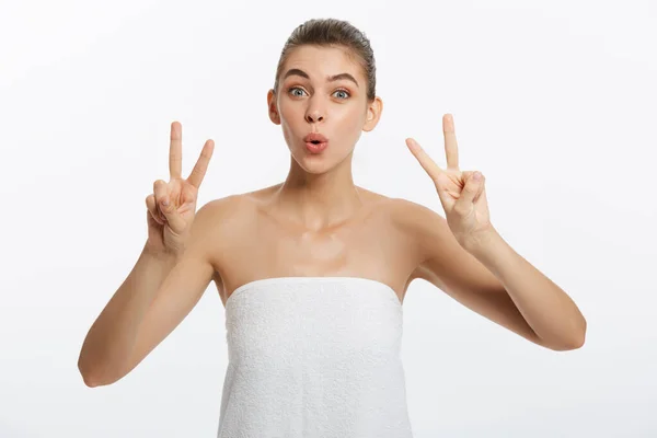 Primo piano di bella giovane donna con asciugamano da bagno che copre il seno, su grigio, mostra due dita segno — Foto Stock