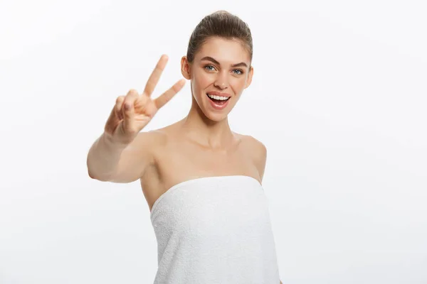 特写的美丽的年轻女子用浴巾覆盖她的乳房, 在灰色, 显示两个手指标志 — 图库照片