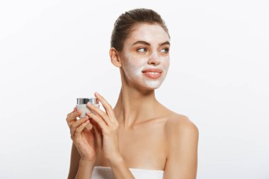 Genç kadının yüzünde beyaz arka plan üzerinde izole krem koymak.