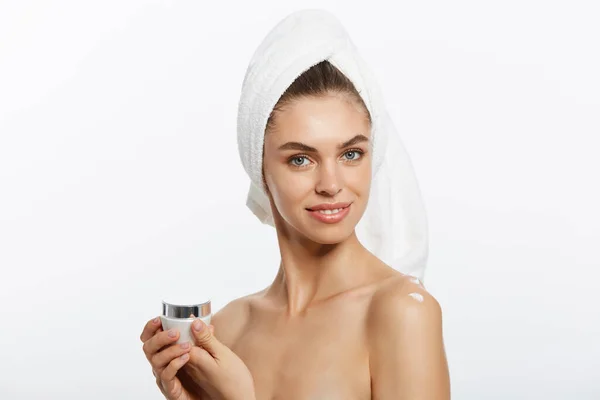 若い女性は、彼女の肌に保湿クリームを適用します。白いバスローブとタオルの白い背景の上の女性の写真。肌ケアのコンセプト — ストック写真