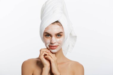 Genç kadının yüzünde nemlendirici krem uygulamak. Kadın beyaz bornoz ve havlu beyaz arka plan üzerinde fotoğrafı. Cilt bakım kavramı