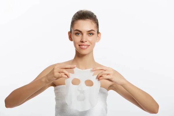 Молодая девушка в маске смотрит в камеру на белом фоне. Косметическая процедура. Косметология и косметология — стоковое фото