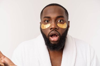 Yüzünde kağıt göz maskesi olan genç bir adam beyaz arka planda soyutlanmış, ağzı açık bir şekilde şoka uğramış görünüyor..