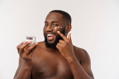 Afrikalı yakışıklı adam yüzüne krem sürüyor. Cilt bakımı kavramı