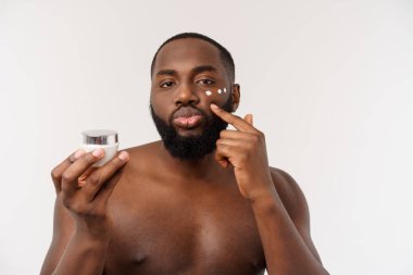 Afrikalı yakışıklı adam yüzüne krem sürüyor. Cilt bakımı kavramı