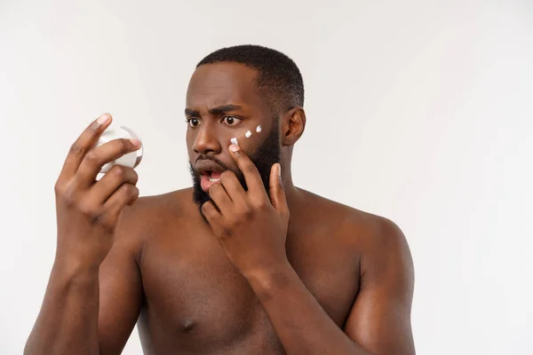 Hombre guapo africano aplicándose crema en la cara. Concepto para el cuidado de la piel —  Fotos de Stock