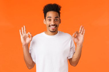 Adam performanstan memnun kalmış. Mutlu Afro-Amerikalı beyaz tişörtlü adam tamam jest yap, sana katılıyorum, gülümse kabul planı, onayla, ürün tavsiye et, tamam de.