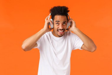 Komşuların iğrenç müzik zevkine ve gürültüsüne katlanamıyor. Kulaklıklarını takıp en sevdiği şarkıları söylüyor. Çalma listesini dinliyor, rahatsız ve tatminsiz turuncu arka plana bakıyor..