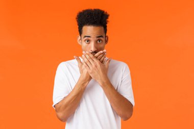 Tanrım, ben ne yaptım? Utanmış ya da garip genç şokta, nutku tutulmuş Afro-Amerikan erkek ağzı kapalı ve utangaç görün, dil sürçmesi, gizli birine anlatmış, turuncu arka plan.