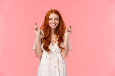 Kendine güvenen, iyimser ve umut dolu beyaz elbiseli, umut dolu kızıl saçlı kadın, şans dileyin ve gülümseyin, dilek tutun, beklenen rüyayı gerçekleştirin, pembe arka planda durun..