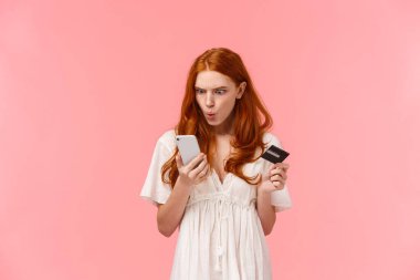 Sinirli ve kızgın, kafası karışmış kızıl saçlı kadın akıllı telefon görüntüsünden memnun değil, bir şeylerin yanlış gittiğinden şikayet ediyor, banka hesabını boş kontrol ediyor, elinde kredi kartı tutuyor..