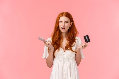 Sinirli ve sinirli kızıl saçlı bir kız, garip online bankacılık sisteminden memnun değil, siparişini alamıyor, elinde akıllı telefon ve kredi kartı ile rahatsız oluyor..