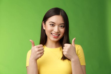Destekleyici Asyalı kız arkadaş sevgili gösterisi onaylama işareti arıyor, neşeli bir şekilde gülümsüyor, iyi bir seçim gibi, mükemmel çabayı kabul ediyor, arkadaşını cesaretlendiriyor, yeşil arka planda duruyor. Boşluğu kopyala