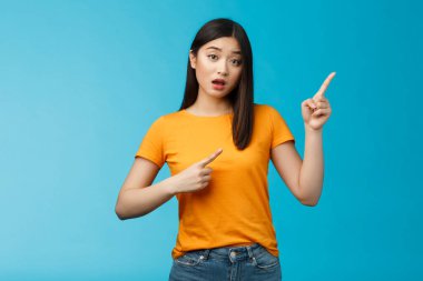 Meraklı, meraklı Asyalı, soru soran aptal, hassas kız ağzını açtı, ilgili bir bakış attı, sağ üst köşedeki şaşkın, mavi arka planı işaret etti. Boşluğu kopyala