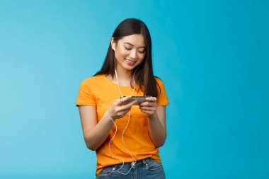 Mutlu Asyalı tatlı kız esmer, kulaklık takıyor kafede en sevdiği akıllı telefon oyununu oynarken rahatsız etmiyor, telefonu yatay tutuyor, gülümsüyor cep telefonu ekranına bakıyor..
