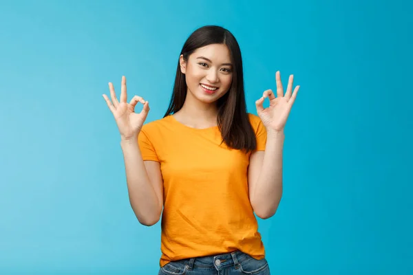 You are perfect. Good-looking cheerful asian girl, show okay ok sign, promote self-acceptance, smiling broadly judging, give positive reply, agree your idea, approve plan, stand blue background.