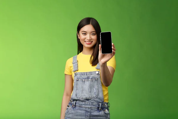 自信自信 英俊的亚洲女性引入智能手机应用 伸出手来 愉快地微笑 推荐社交形象 吹嘘自己的博客 绿色背景 — 图库照片
