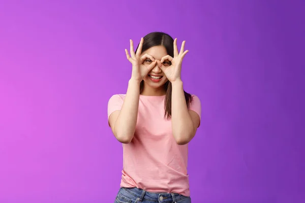 Cheerful friendly carefree asian woman having fun fool around, show okay ok signs on eyes make glasses from fingers, smiling delighted, mimicking funny emotions, stand purple background happy.