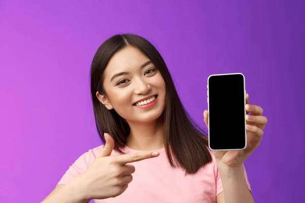 特写欢快迷人的亚洲女人斜着头可爱 现在的应用程序 显示智能手机显示介绍应用程序 指向电话显示食指屏幕 站在紫色背景 — 图库照片