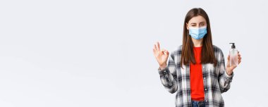 Coronavirus salgını, karantina, sosyal mesafeler ve duygu kavramı. Hiç sorun değil. Tıbbi maskeli hoş kız el dezenfektanı gibi işaret ve göz kırp..