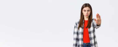 Yaşam tarzı, farklı duygular, boş zaman aktiviteleri konsepti. Durma zamanı. Sıradan giyinmiş ciddi bir genç kadın, yasaklamak, yasaklamak ya da yasaklamak için elini uzat, beyaz arka plan..