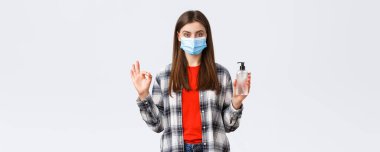 Coronavirus salgını, karantina, sosyal mesafeler ve duygu kavramı. Sağlık maskeli memnun genç bayan bu el dezenfektanı markasını almanı tavsiye ediyor..