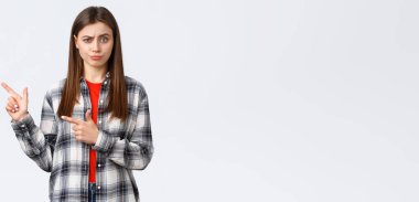 Yaşam tarzı, farklı duygular, boş zaman aktiviteleri konsepti. Şüpheci ve etkilenmemiş kızın şüpheci düşünceleri, şüpheciliği ve şüpheciliği ifade eder, parmaklarını sola uzatır ve hoşnutsuzca sırıtır..