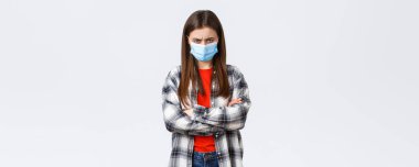 Coronavirus salgını, karantina, sosyal mesafeler ve duygu kavramı. Tıbbi maskeli kızgın genç kız arkadaş ve günlük gömleği kontrol et, alınma, somurt ve savunmaya geç..