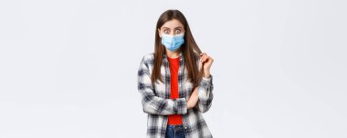 Coronavirus salgını, karantina, sosyal mesafeler ve duygu kavramı. Şok olmuş ve meraklı maskeli genç kız gömleğini kontrol ediyor, dedikodu yapan arkadaşına bakıyor ya da çarpıcı haberler veriyor..