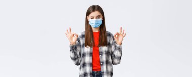 Coronavirus salgını, karantina, sosyal mesafeler ve duygu kavramı. Tıbbi maskeli kararlı genç bir kadın, her şeyin yolunda olduğuna emin ol, tamam işaretler ve göz kırp, sorun yok..