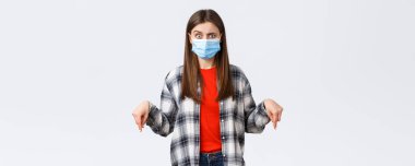 Coronavirus salgını, karantina, sosyal mesafeler ve duygu kavramı. Tıbbi maskeli kafası karışmış bir kadın ne olduğunu anlayamaz, işaret eder, alarma geçer..