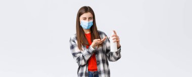 Coronavirus salgını, karantina, sosyal mesafeler ve duygu kavramı. Tıbbi maskeli tatlı bir kadın, el dezenfektanı ya da sabun sürerken sana göz kırpıyor, virüsü engelliyor..