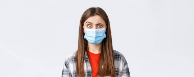 Coronavirus salgını, karantina, sosyal mesafeler ve duygu kavramı. Tıbbi maskeli kafası karışmış ve ürkmüş bir kız garip bir şey gördüğünde, kaşlarını kuşkulandırır..