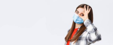 Coronavirus salgını, karantina, sosyal mesafeler ve duygu kavramı. Medikal maskeli tatlı kız, her şeyin yolunda olduğunu gösteriyor, tamam işaretini gözünün üstüne koy..