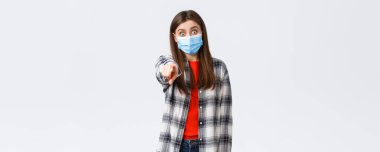 Coronavirus salgını, karantina, sosyal mesafeler ve duygu kavramı. Şaşırmış ve etkilenmiş, heyecanlı kız birini tanıyor, kamerayı işaret ediyor, tıbbi maske takıyor..