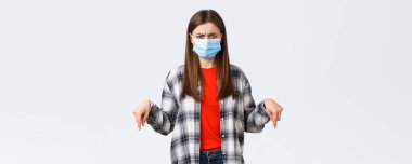 Coronavirus salgını, karantina, sosyal mesafeler ve duygu kavramı. Hayal kırıklığına uğramış ve kızgın genç bir kadın bunu tasvip etmiyor, parmakları aşağıda ve kaşlarını çatarak yargılıyor..