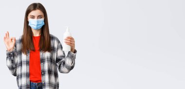 Coronavirus salgını, karantina, sosyal mesafeler ve duygu kavramı. Kendine güvenen tıbbi maskeli genç bir kadın el sabunu ya da dezenfektan tavsiye ediyor..