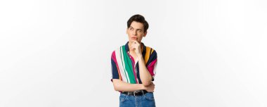 Yakışıklı, sol üst köşeye bakan, düşünen ya da seçim yapan, beyaz arka planda duran eşcinsel bir adam resmi..