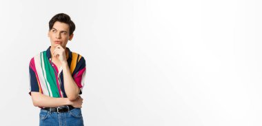 Yakışıklı, sol üst köşeye bakan, düşünen ya da seçim yapan, beyaz arka planda duran eşcinsel bir adam resmi..