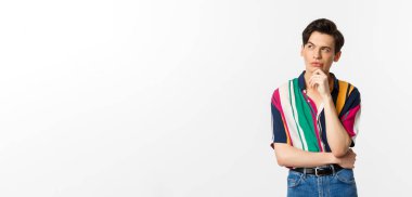 Yakışıklı, sol üst köşeye bakan, düşünen ya da seçim yapan, beyaz arka planda duran eşcinsel bir adam resmi..