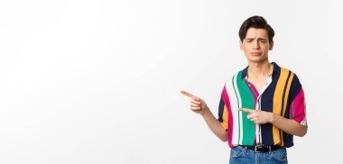 Şüpheci, küçümseyici bakışları olan ve sol elini gösteren, onaylamayan ve sevmeyen, beyaz arka planda duran eşcinsel bir adam..