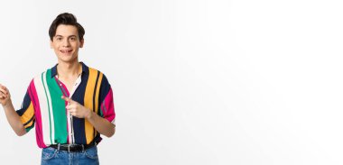 Şık giyinmiş yakışıklı bir gencin portresi, solu işaret ediyor ve gülümsüyor, reklamını yapıyor, beyaz arka planda duruyor..