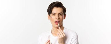 Yüzünde sim olan, dudak parlatıcısı süren, kameraya bakan, beyaz arka planda duran, cinsiyet değiştiren kişilere yakın çekim..